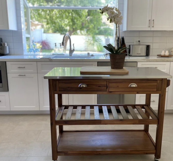A wooden kitchen island adorned with a potted orchid, a cutting board, and drawers, set against a backdrop of a modern kitchen with a large window
