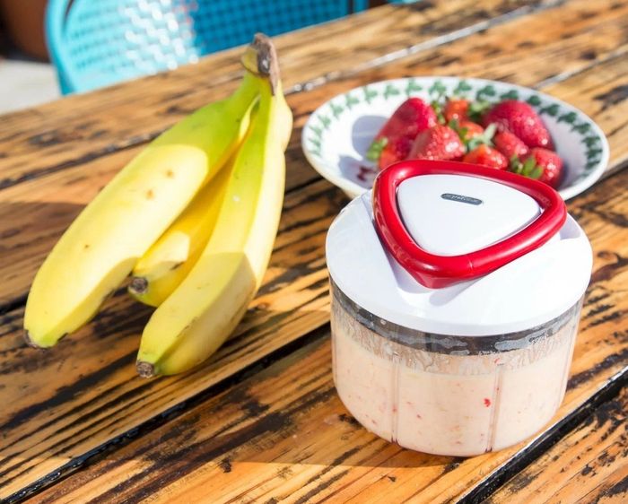 The food processor placed next to strawberries and bananas, with pureed fruit inside
