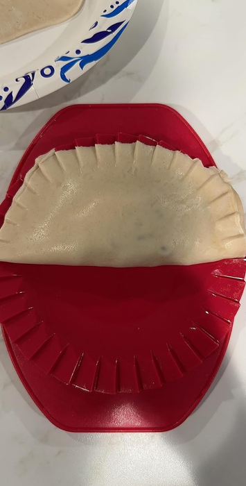 An empanada inside the red dough press, ready to be sealed