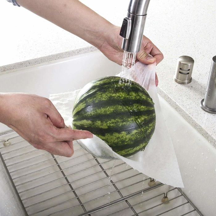 A watermelon being held with a paper towel underneath, with running water streaming over it.