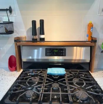 Kitchen stove with a stainless steel backsplash, salt and pepper grinders, a blue dish, and cleaning supplies on either side