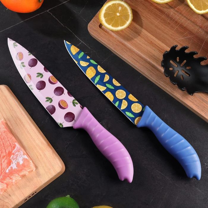Two kitchen knives with fruit-patterned blades, one adorned with a pink handle and the other with a blue handle, resting on a countertop beside a cutting board with lemon and salmon