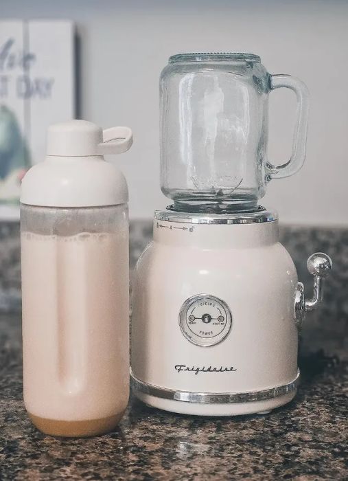 A small white retro-style blender with a glass top and smoothie contents beside it in a water bottle