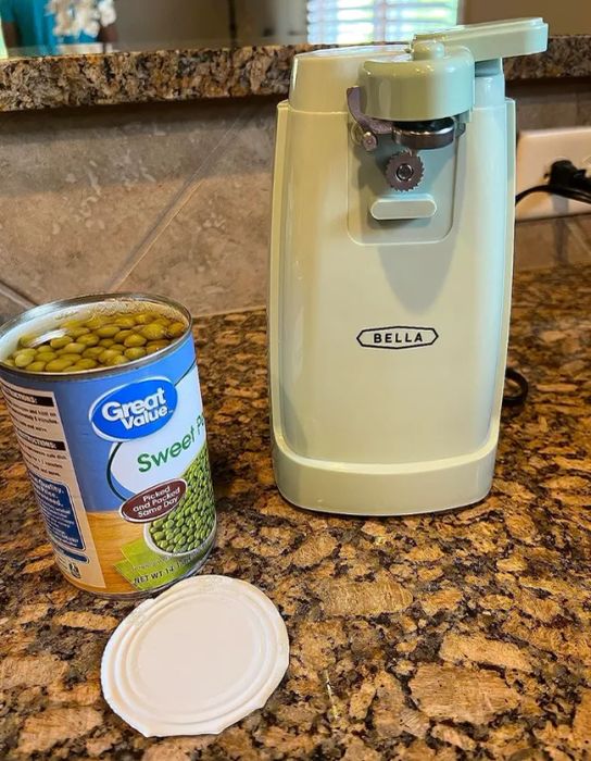A small sage green retro-style can opener sitting beside an open can of peas