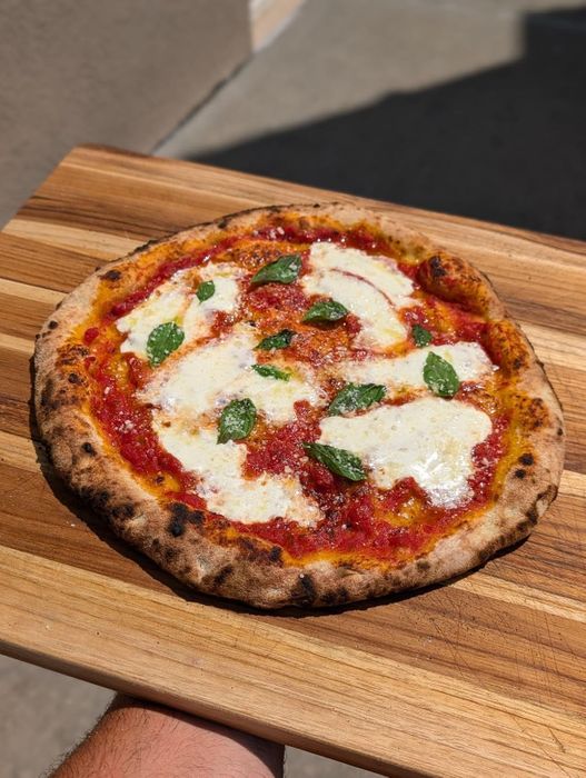 A freshly baked pizza with gooey melted cheese and basil leaves on a wooden board