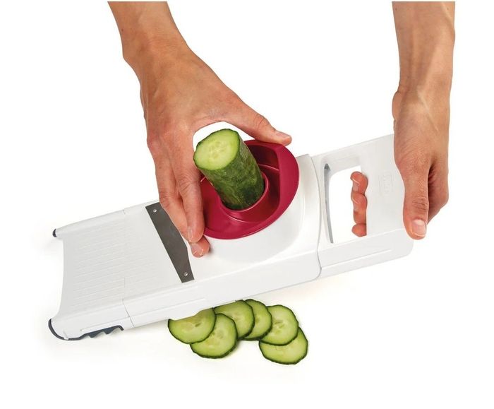 A person slicing a cucumber with a slicing tool