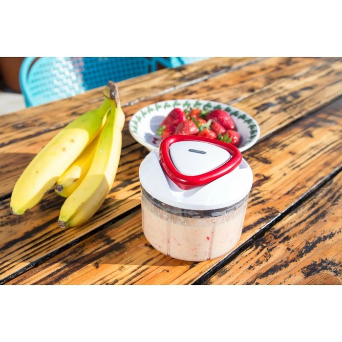 The food processor is placed next to strawberries and bananas, with pureed fruit inside.