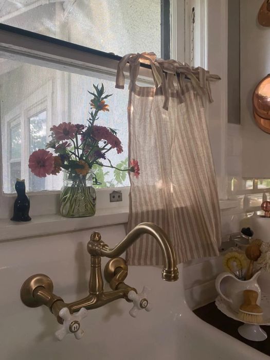 A kitchen sink adorned with a brass faucet and a vase of flowers sitting gracefully on the windowsill.