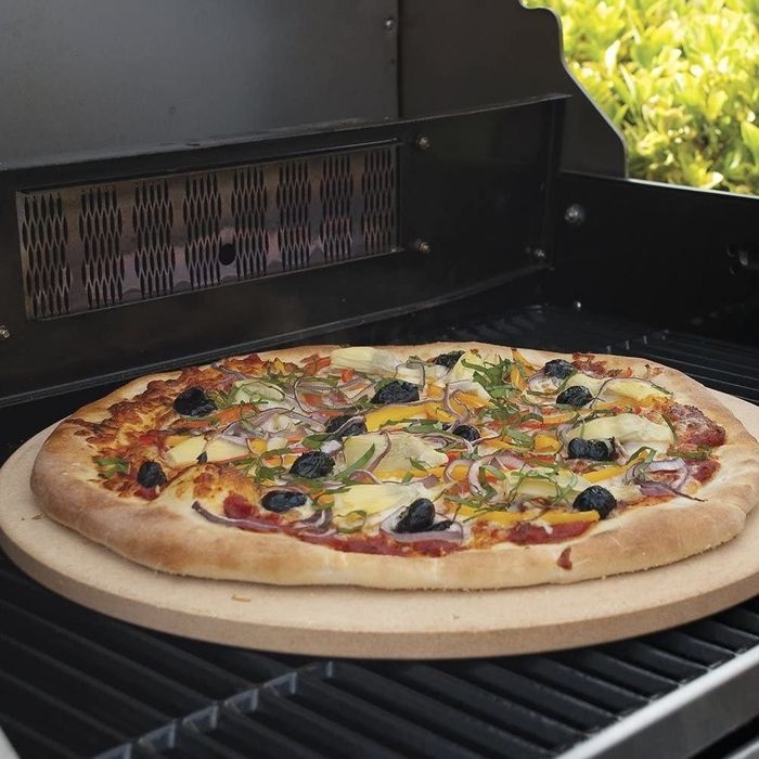 A pizza topped with olives, onions, and other toppings, placed on a pizza stone atop a grill