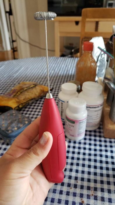 A hand holding a vibrant red milk frother