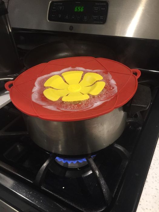 A red silicone cover preventing boiling water from spilling over a pot