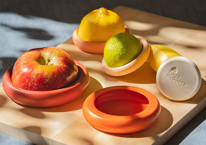 An assortment of different-sized fruits, cut in half, with food huggers placed on the exposed side