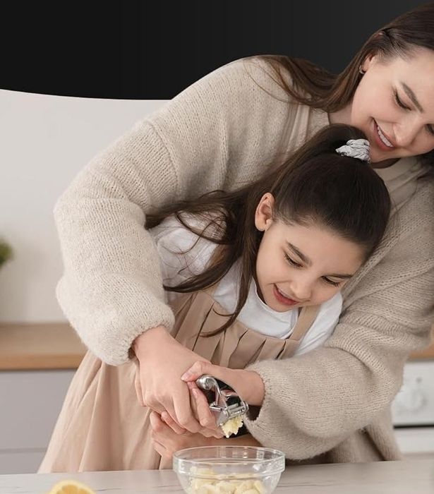 A parent and child using a garlic press in the kitchen
