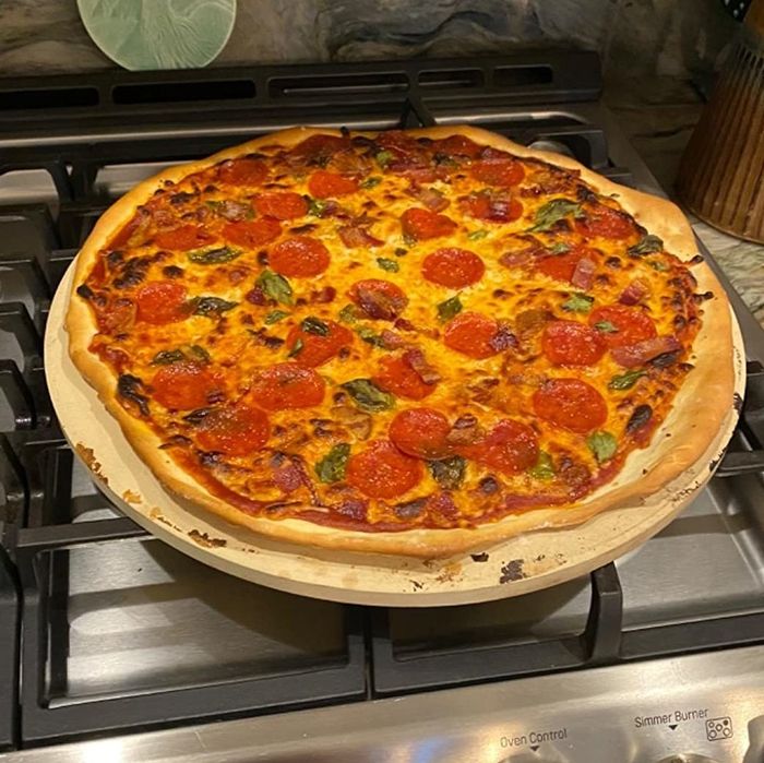 Pepperoni pizza resting on a pizza stone atop a stovetop