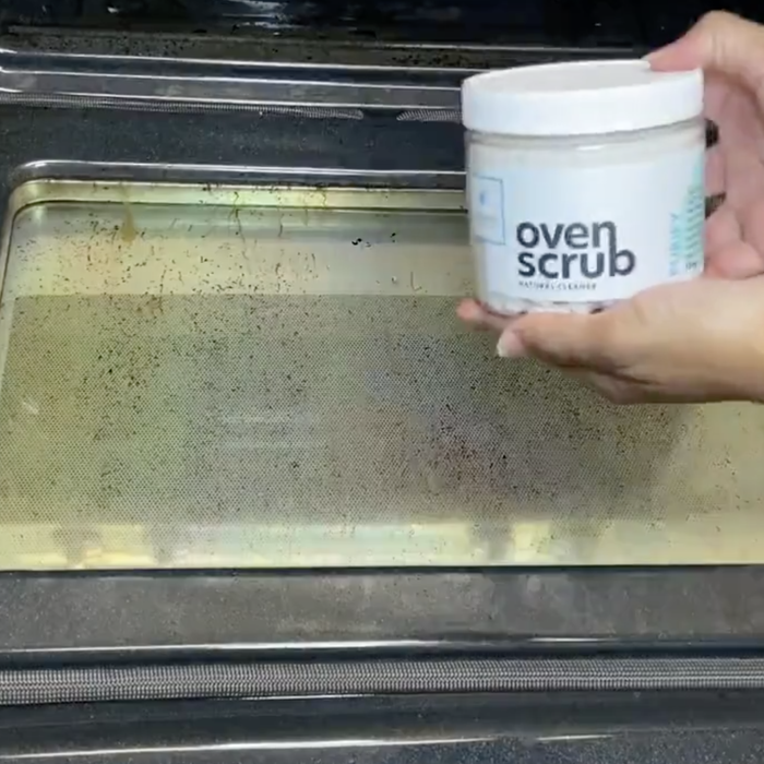 A model holding the Oven Scrub in front of a dirty oven door