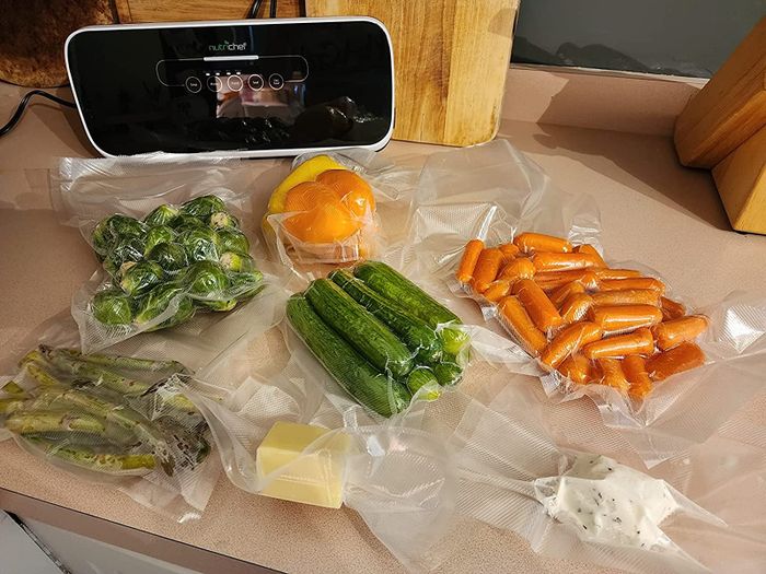 A reviewer photo of the vacuum sealer surrounded by various foods sealed in vacuum bags