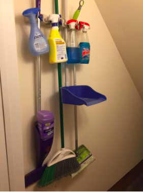Reviewer’s photo of the wall-mounted broom organizer featuring four cleaning tools and four spray bottles neatly arranged