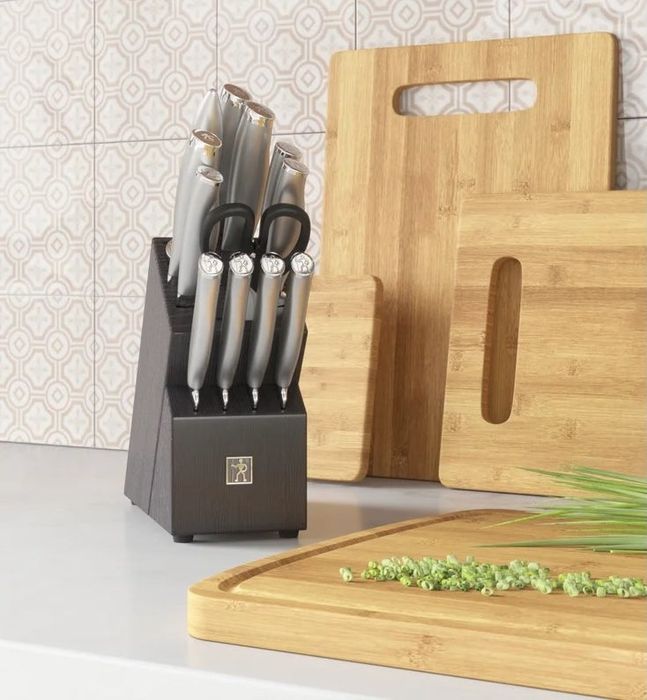 A stainless steel knife set housed in a black knife block placed on a kitchen counter beside a bamboo cutting board