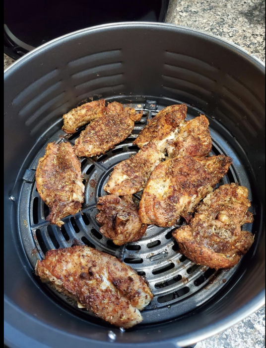 An open air fryer shelf displays fully cooked and seasoned chicken wings.