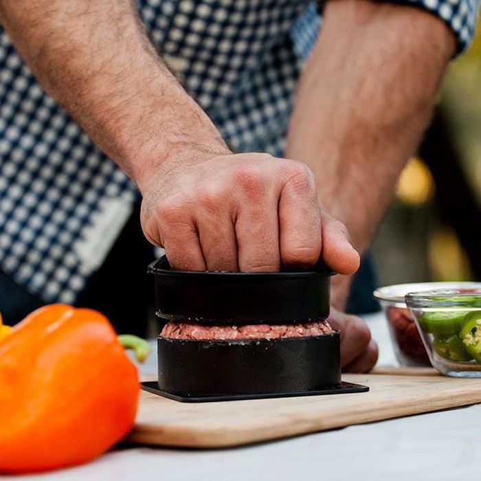 A person using a burger press on a cutting board