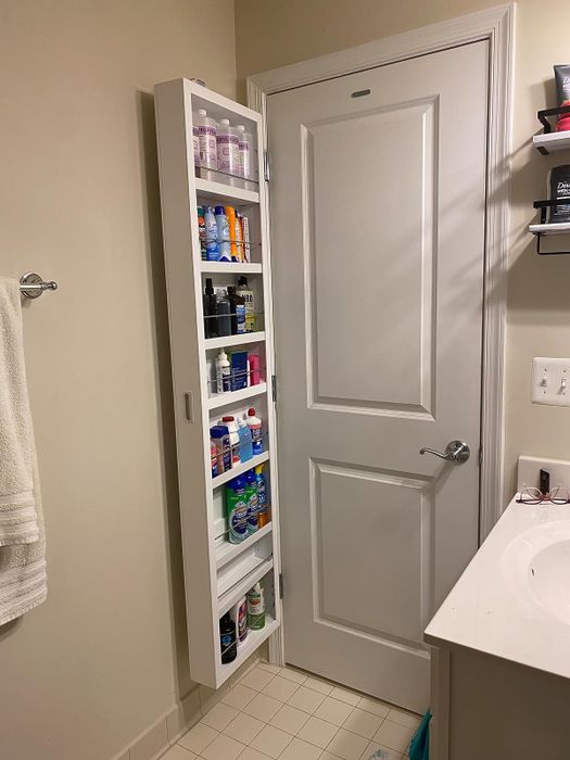 The reviewer's hinged cabinet mounted on the back of a bathroom door, opening to reveal several shelves storing various items.