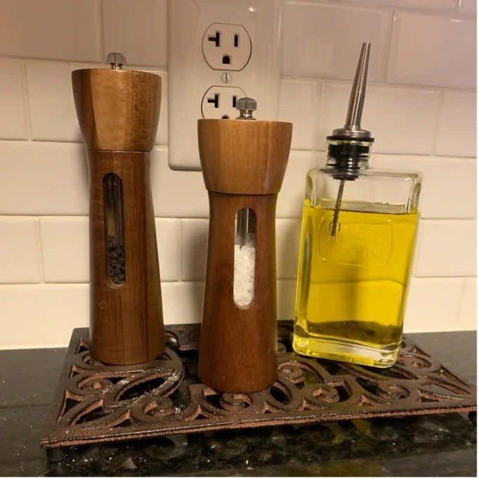 The salt and pepper grinder set displayed next to a bottle of olive oil