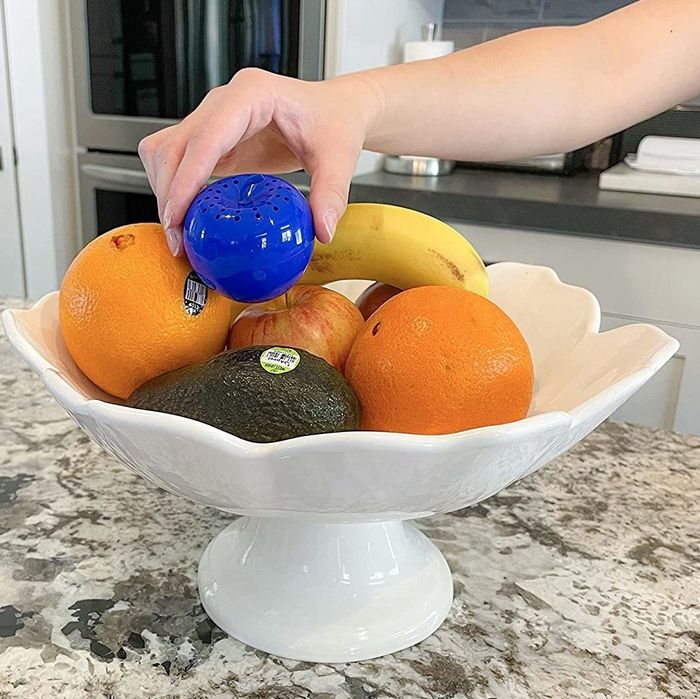 A model placing the apple-shaped produce saver into a bowl of fresh fruit