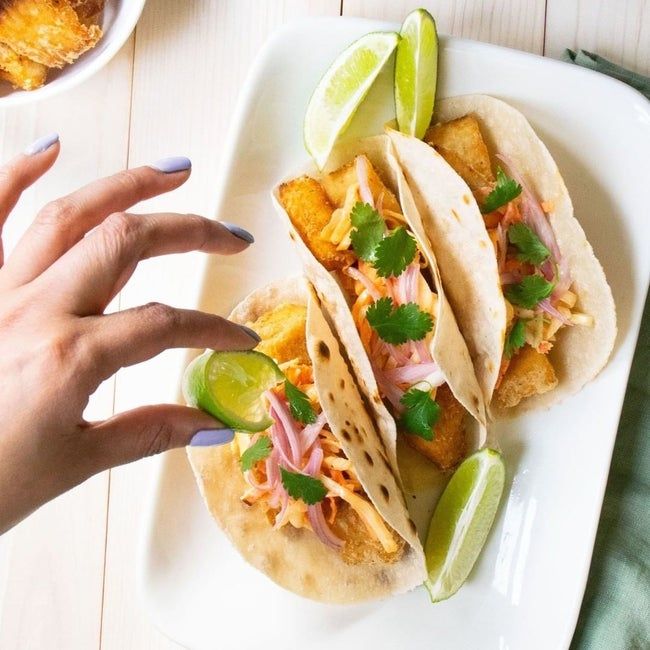 A hand squeezing fresh lime juice onto three tacos, making them even more appetizing.