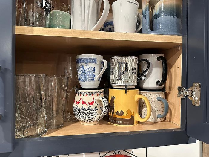 Black mug organizers placed under different mugs inside a cabinet