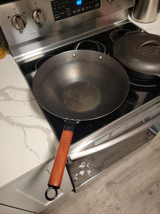 A carbon steel wok with a wooden handle sits on an electric stove.