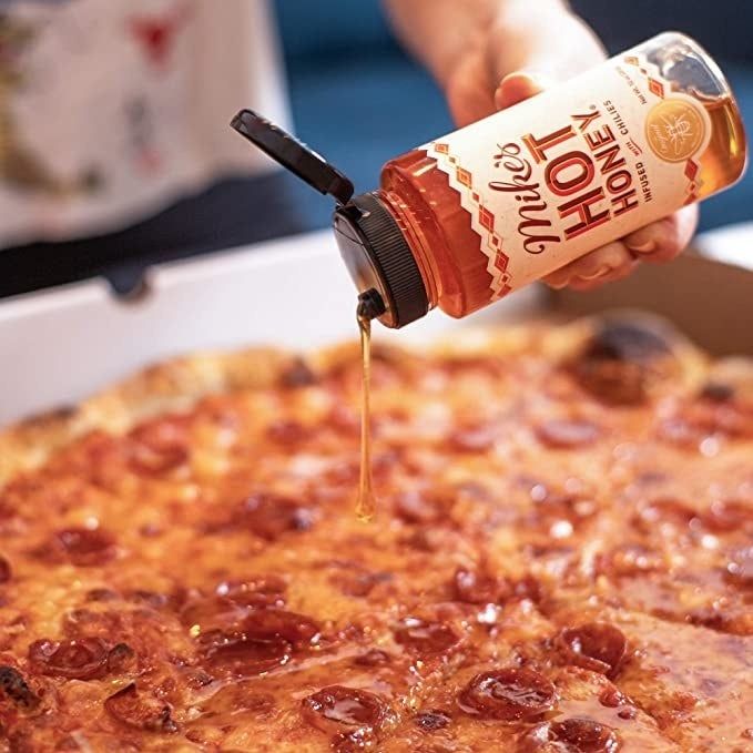 A hand drizzling Mike's Hot Honey over a pepperoni pizza