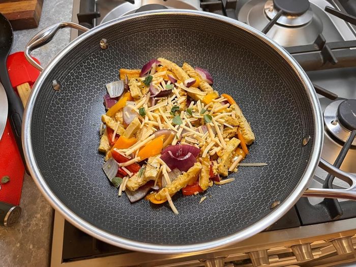 A wok on the stove filled with a stir-fry made from vegetables, tofu, and shredded cheese, indicating a home-cooked meal in the making