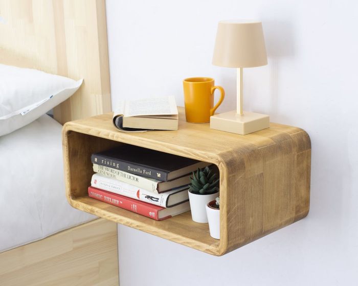 light-colored floating nightstand beside a bed holding a lamp, books, and a coffee mug