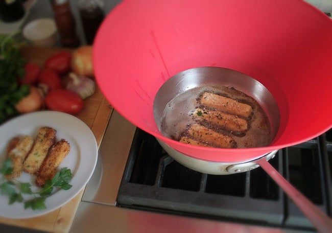 A cooktop with a frying pan, and the cone-shaped splatter guard surrounding it, effectively capturing oil splatters.