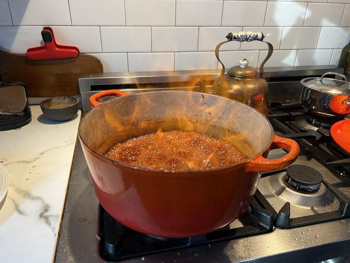 A red Dutch oven bubbling with sauce on a stove