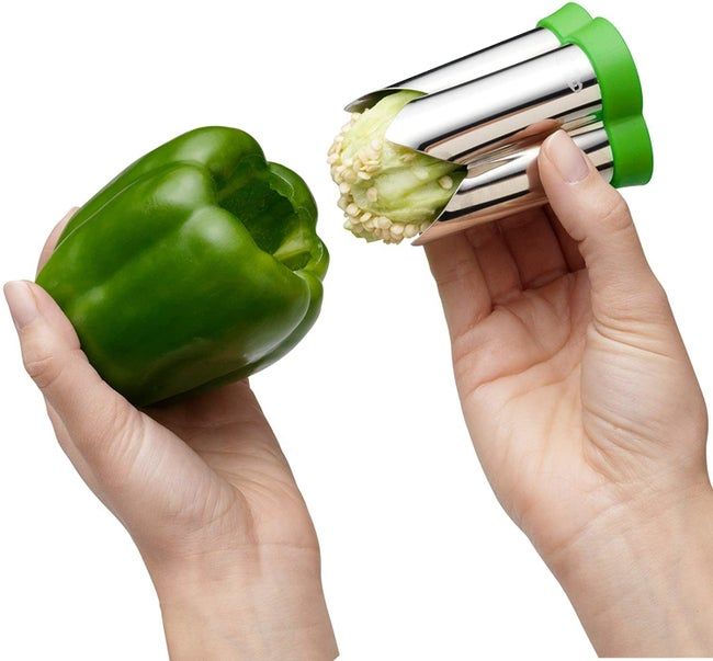 Hands demonstrating the stainless steel corer with the stem and seeds inside, next to a perfectly cored bell pepper.