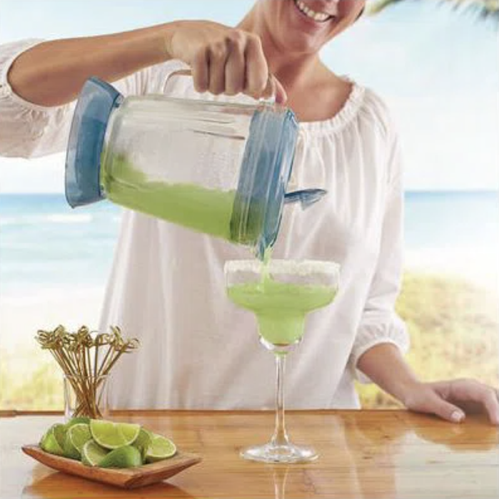 A woman in a white blouse pours a refreshing green drink from a blender into a margarita glass