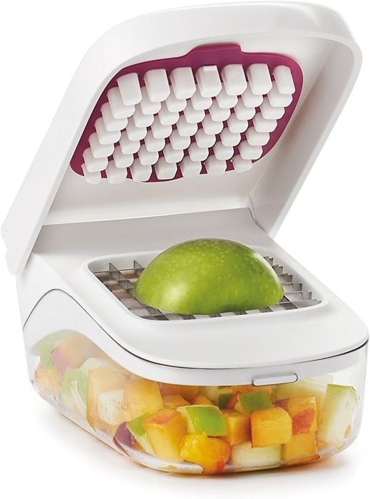 The fruit and vegetable chopper, shown with a green apple being diced, is placed next to a container filled with a mix of chopped fruit and vegetables.