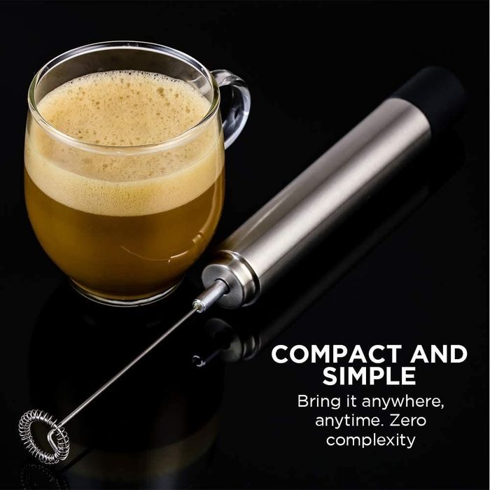 A handheld milk frother placed beside a cup of frothy coffee