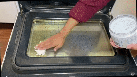 A gif showing someone applying the paste to a dirty oven door and wiping it clean with a cloth.