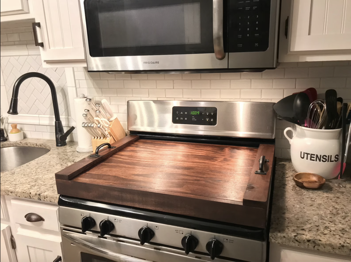 A stove with a dark wood stovetop cover with handles placed on top