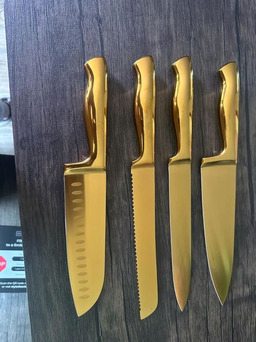 A set of four gold kitchen knives with various blade shapes displayed on a wooden surface