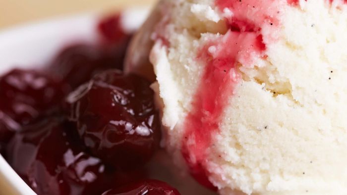 A close-up of a scoop of vanilla ice cream with cherry compote served on the side.