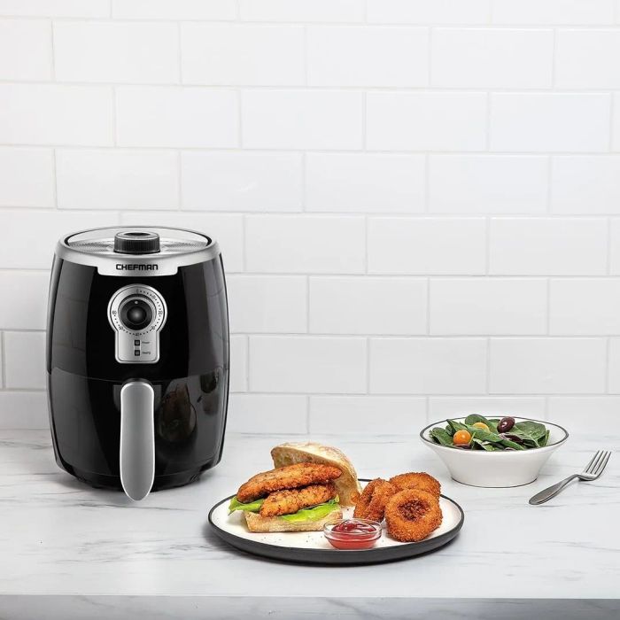 An air fryer positioned beside golden onion rings and a crispy fried chicken sandwich.