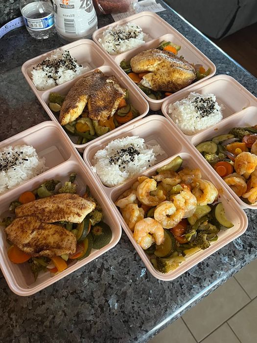 Six meal prep containers filled with grilled fish, shrimp, rice, and a mix of vegetables.