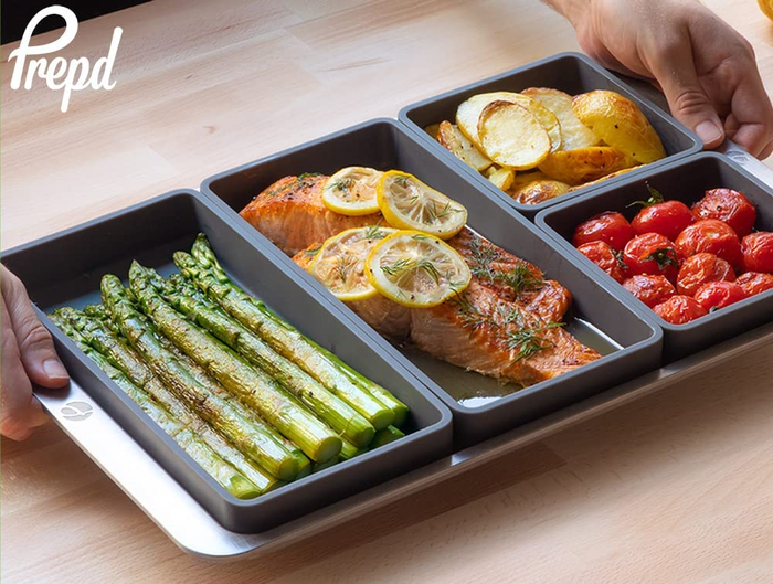 A model holding a sheet pan with four silicone dividers, each filled with a different type of food