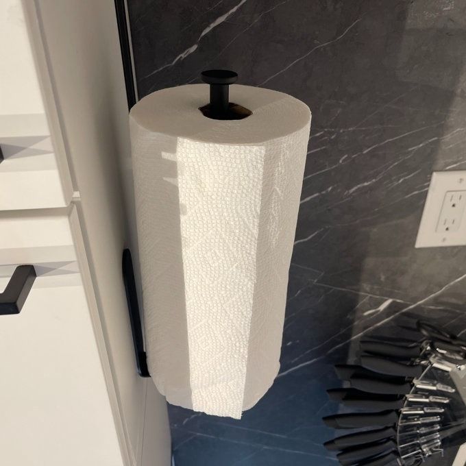 Photo from a reviewer showing a roll of paper towels mounted on a sleek black wall holder in a modern kitchen setting.