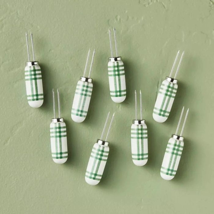 A set of eight corn holders featuring green and white plaid handles, neatly arranged on a flat surface.