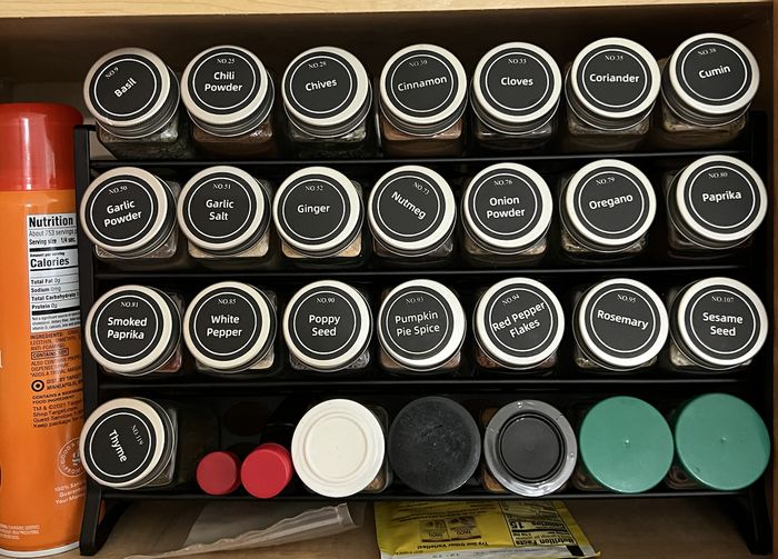 A spice rack stocked with jars labeled for spices like Basil, Chili Powder, and Cinnamon, along with additional bottles and containers surrounding the rack.