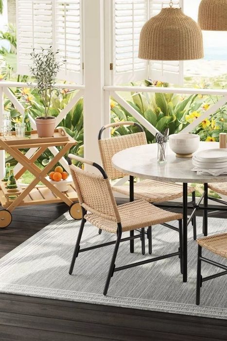 An outdoor patio featuring a round dining table, four wicker chairs, hanging lights, and the stylish serving cart placed beside it